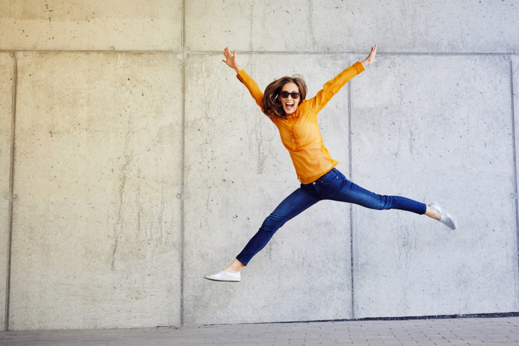 Original stock image of woman jumping in front of a wall.